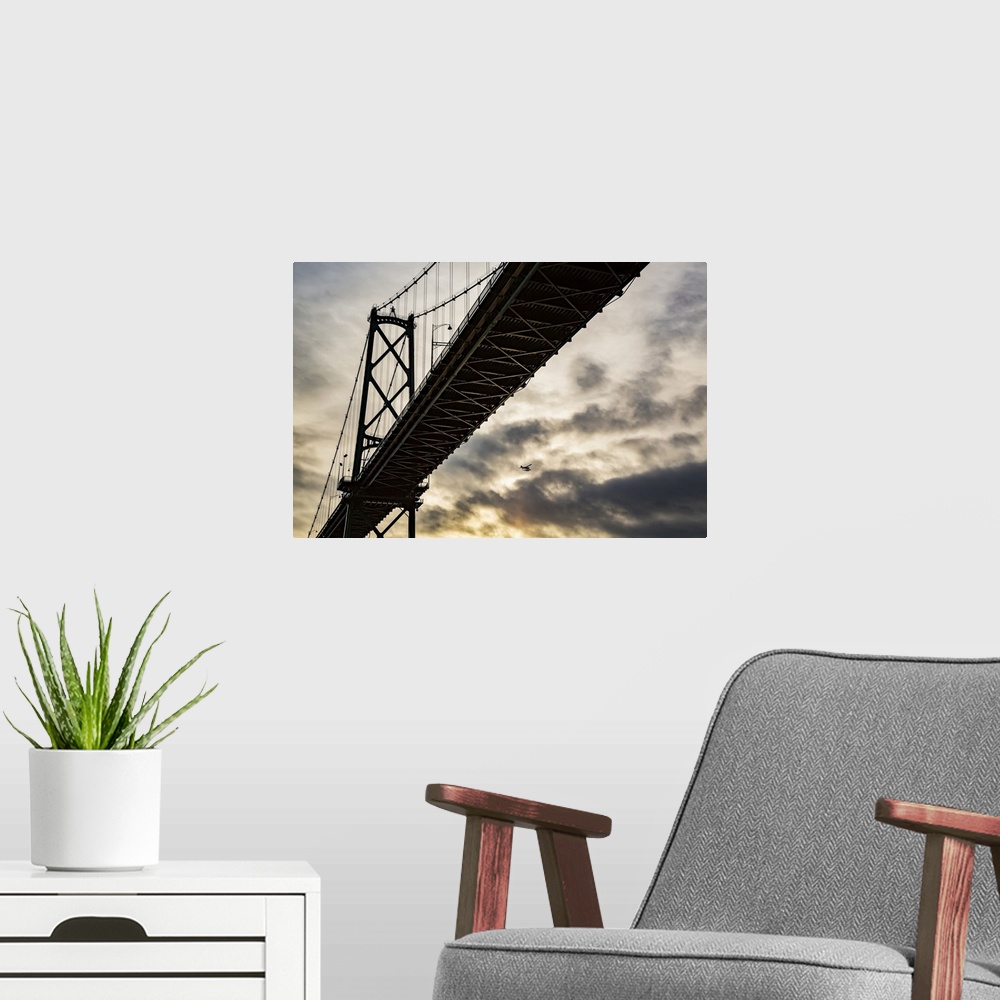 A modern room featuring Low angle view of a bridge at sunset with an airplane flying in the distance; Vancouver, British ...