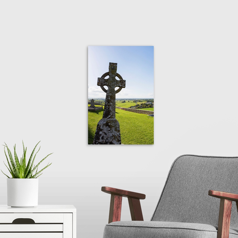A modern room featuring Celtic cross on grassy hill with stone wall under blue sky, Cashel, County Tipperary, Ireland.