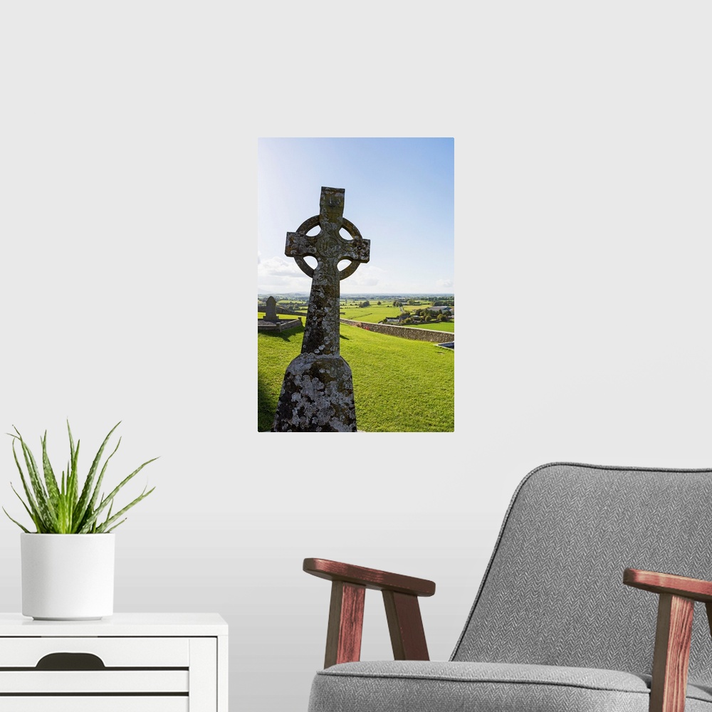A modern room featuring Celtic cross on grassy hill with stone wall under blue sky, Cashel, County Tipperary, Ireland.