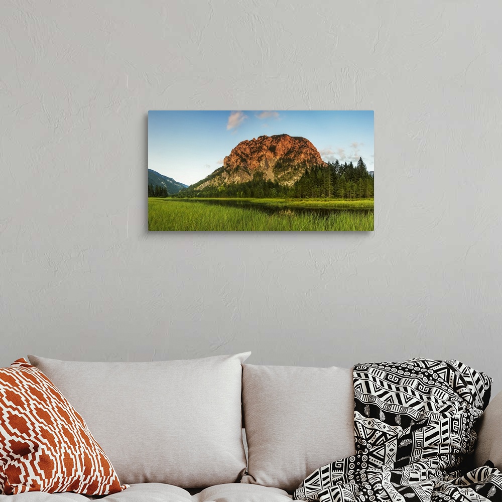 A bohemian room featuring Cliff face on alpine mountain being hit with a summer evening sun, overlooking a lake and forest;...