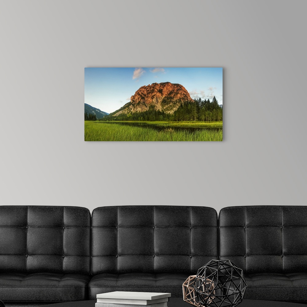 A modern room featuring Cliff face on alpine mountain being hit with a summer evening sun, overlooking a lake and forest;...