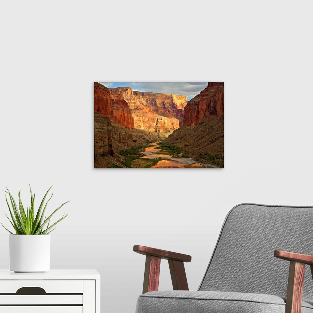 A modern room featuring Large wall art of a river winding through the bottom of the Grand Canyon while the sides of the c...