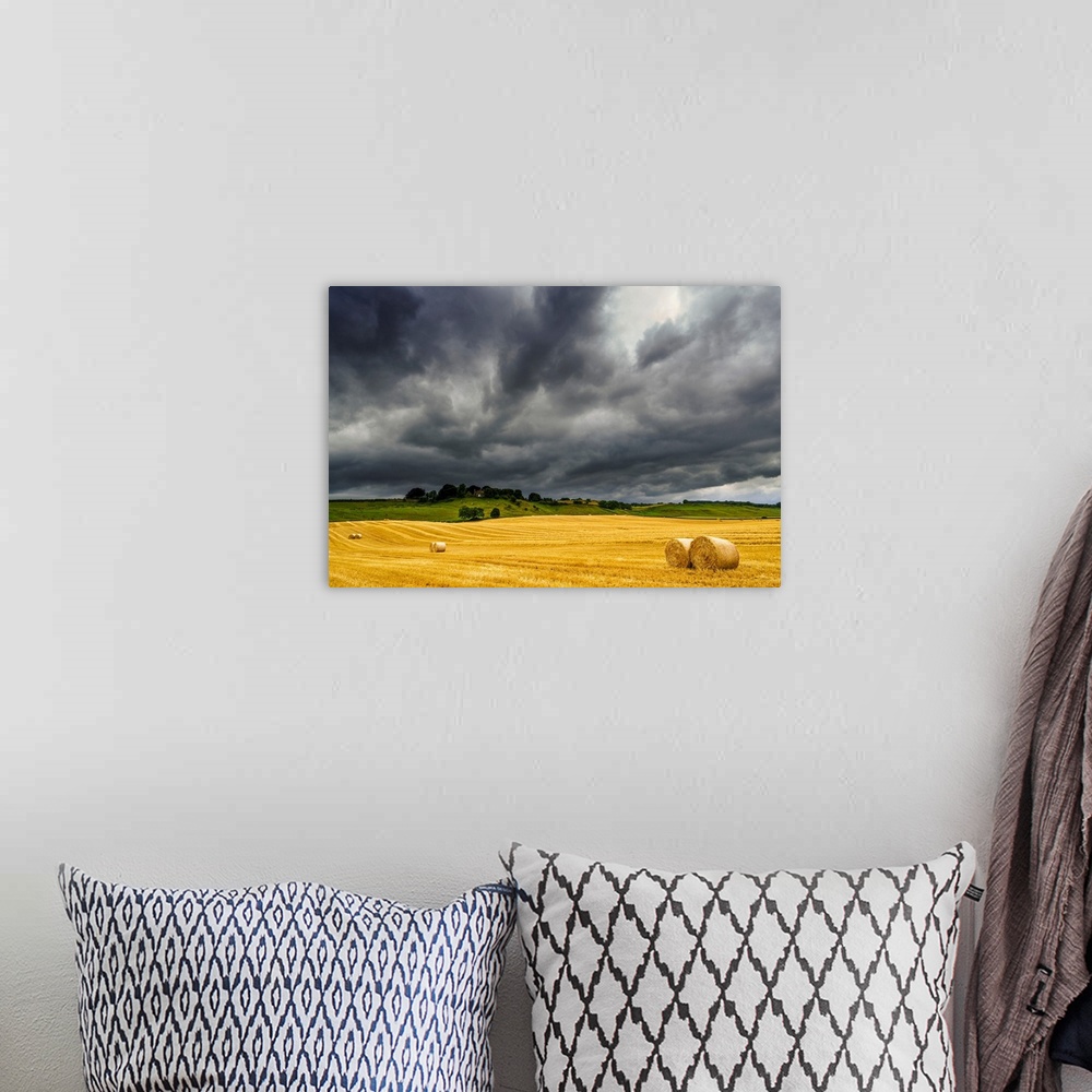 A bohemian room featuring Dark storm clouds roll over a golden farm field with hay bales; Ravensworth, North Yorkshire, Eng...