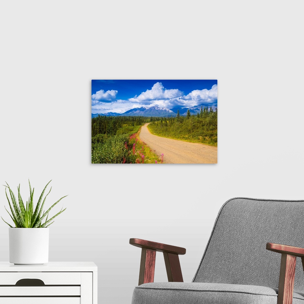 A modern room featuring Landscape photograph on a big canvas of a dirt road curving through a forest of pines and wildflo...