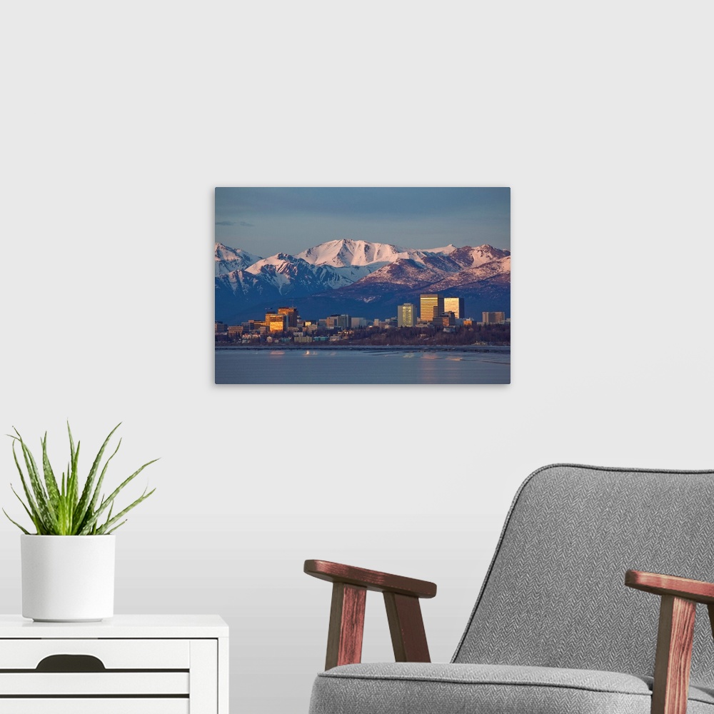 A modern room featuring Chugach mountain range seen behind a wide angle view of downtown Anchorage with mudflats in the f...