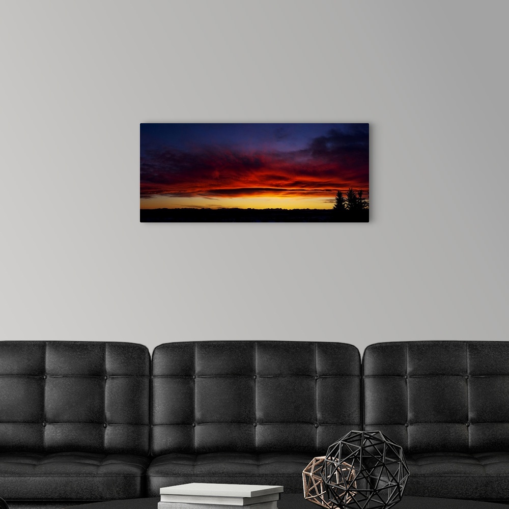 A modern room featuring Dramatic colourful sky/clouds at sunset with silhouette trees and mountain range in background; C...