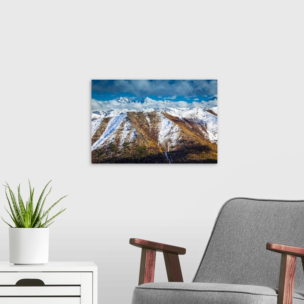 A modern room featuring Fall coloured Chugach Mountains dusted with snow, jagged peaks in the background. Chugach State P...