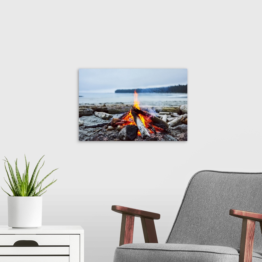 A modern room featuring A fire on the beach with the ocean and coastline in the background, Cape Scott Provincial Park; B...