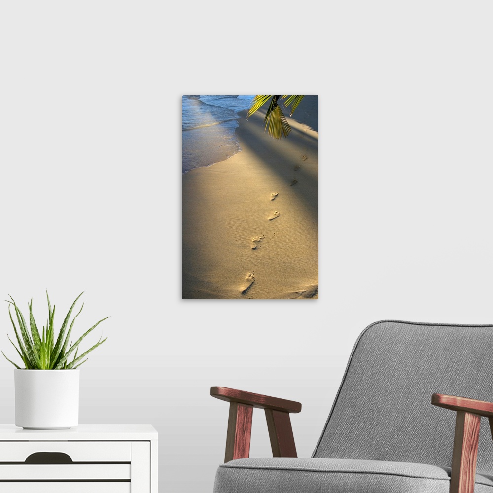 A modern room featuring Vertical photograph on a large wall hanging of a single row of footprints in the sand, near the s...
