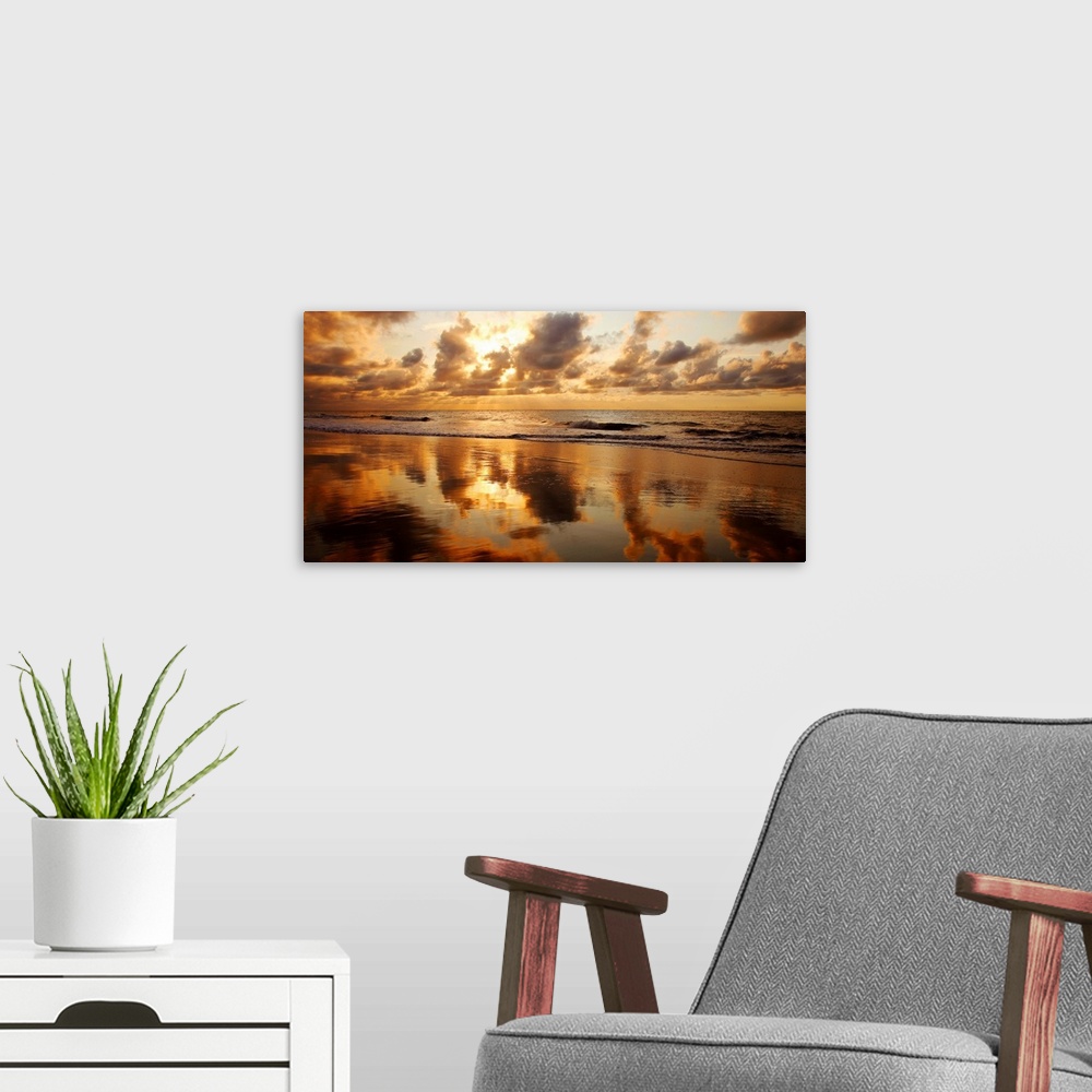 A modern room featuring Panoramic photograph of seashore at dusk.  There is standing water on the beach and waves rolling...