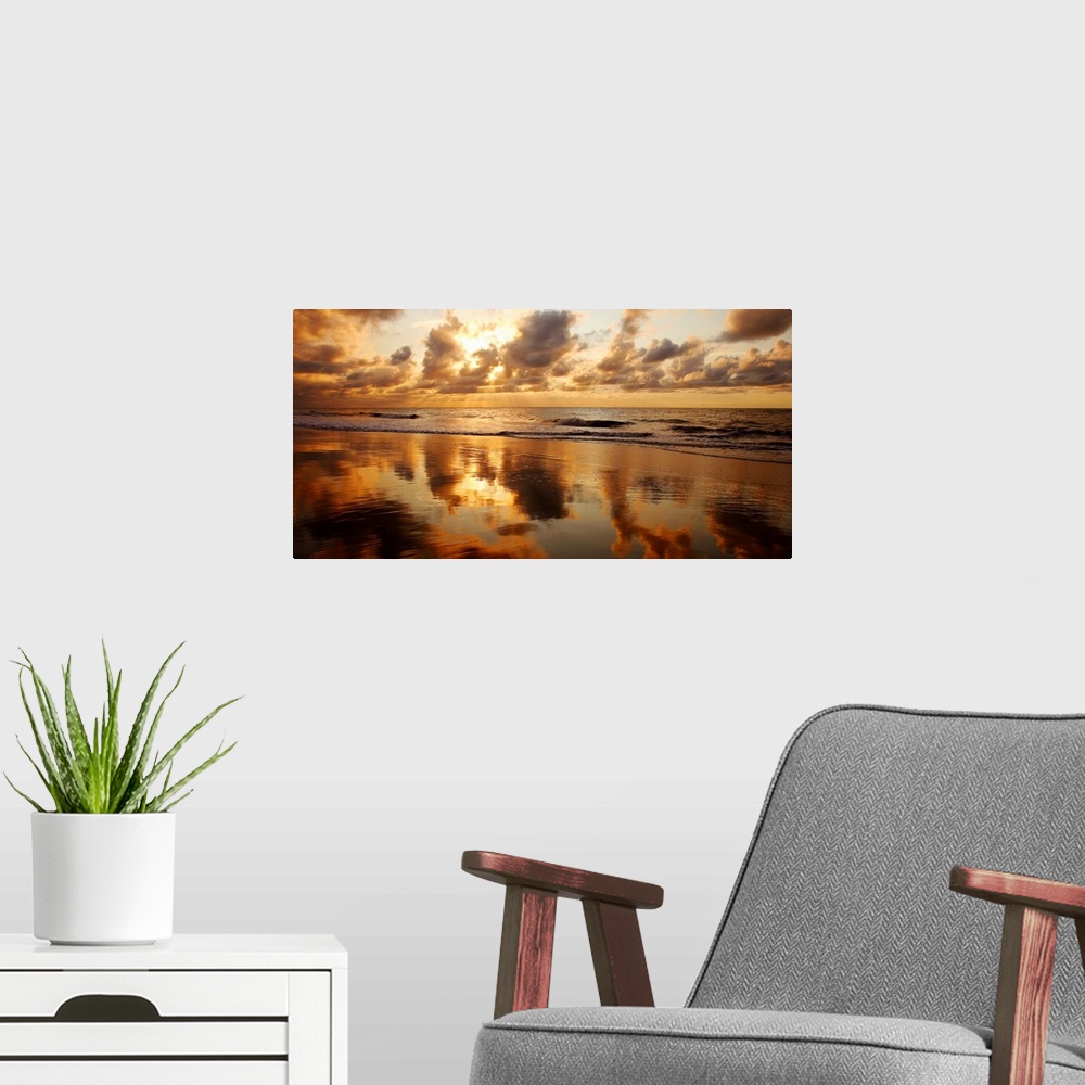 A modern room featuring Panoramic photograph of seashore at dusk.  There is standing water on the beach and waves rolling...