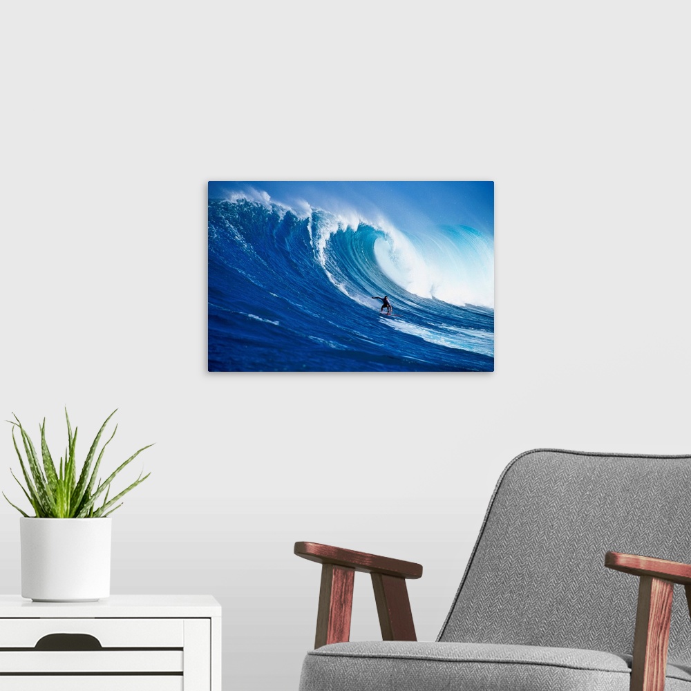 A modern room featuring A lone figure on a surfboard coasts down the side of a huge wave as it crests over him, filling t...