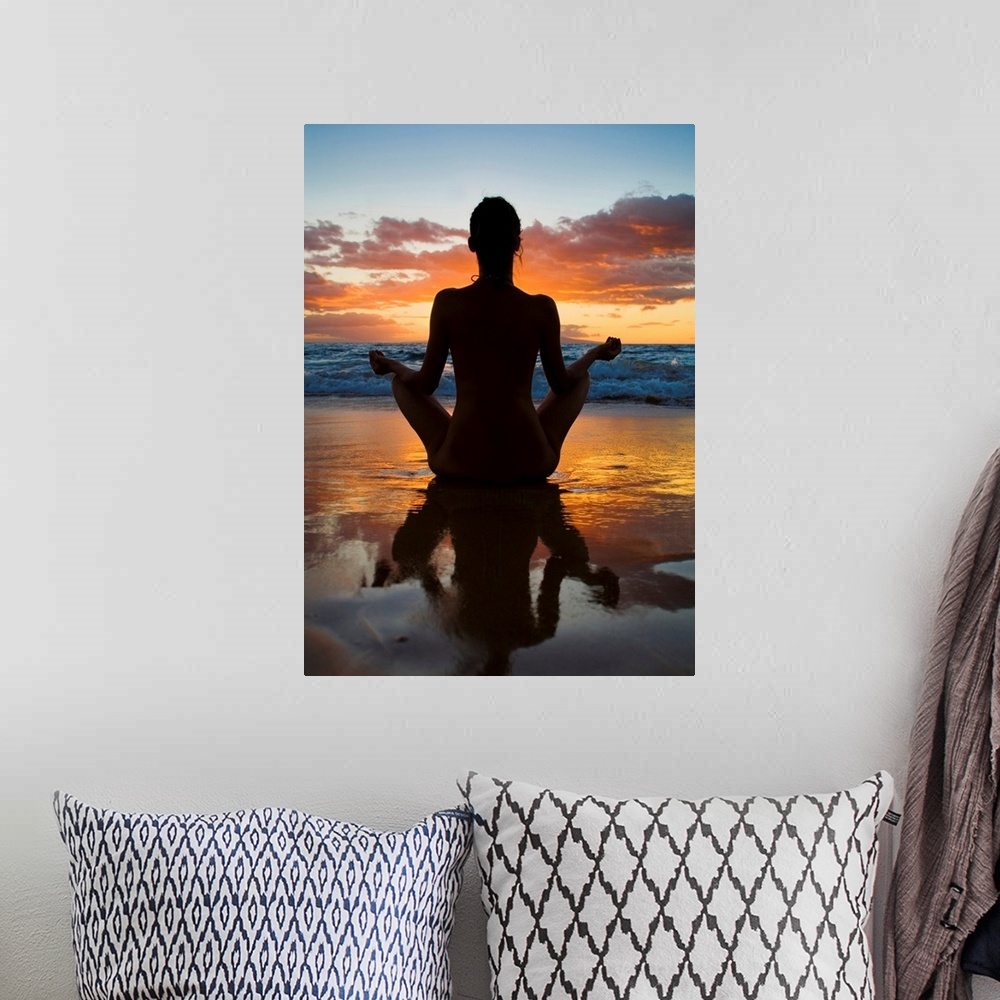 A bohemian room featuring Woman meditating and doing yoga on the wet sand as the surf breaks in front of her and the sun se...