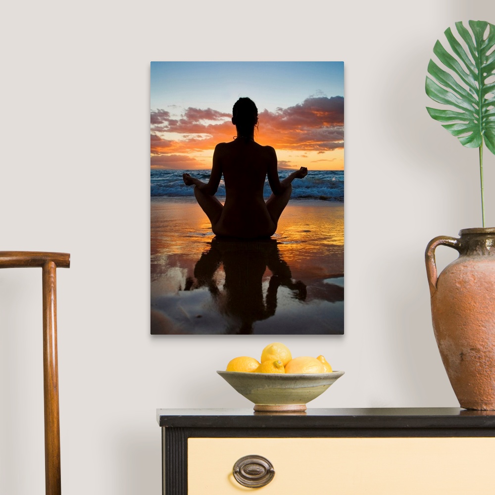 A traditional room featuring Woman meditating and doing yoga on the wet sand as the surf breaks in front of her and the sun se...