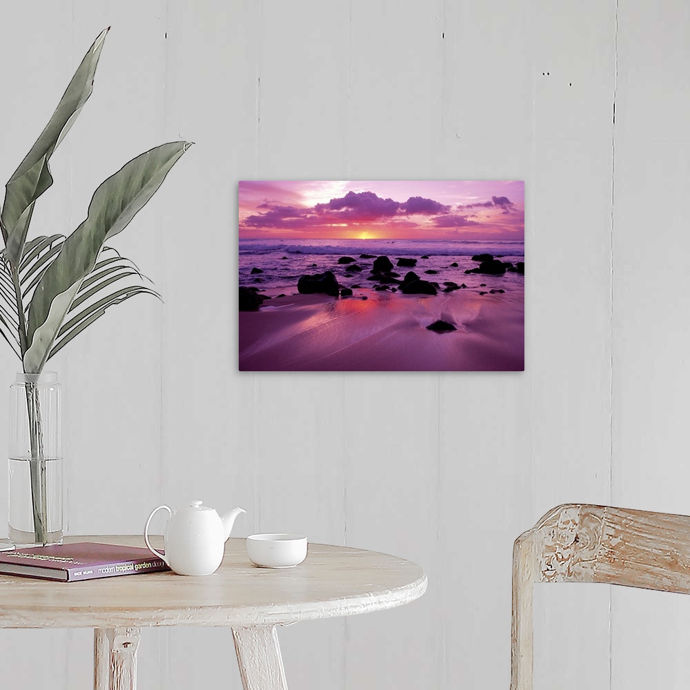 A farmhouse room featuring Several dark rocks dot the beach among shallow waves at twilight as purple clouds loom overhead.