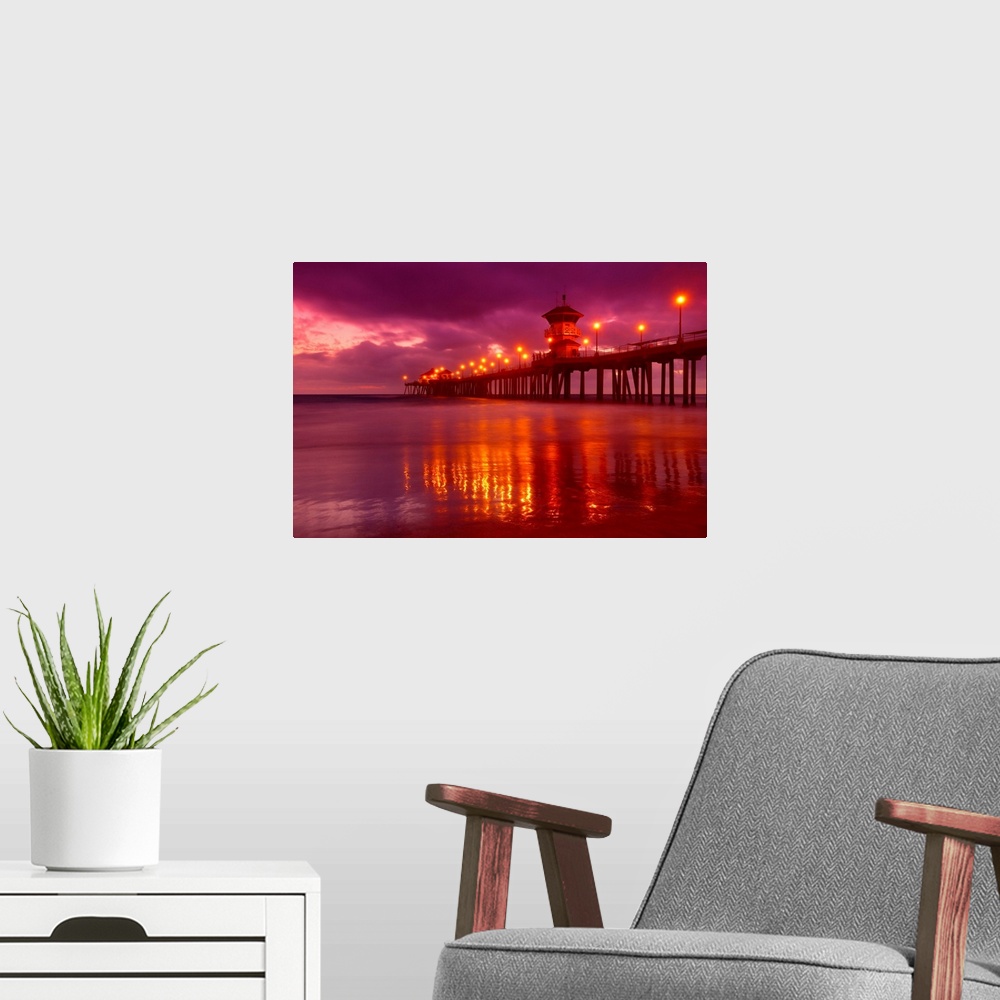 A modern room featuring Big horizontal photograph of a lit pier reflecting in the water near Huntington beach at dusk, be...