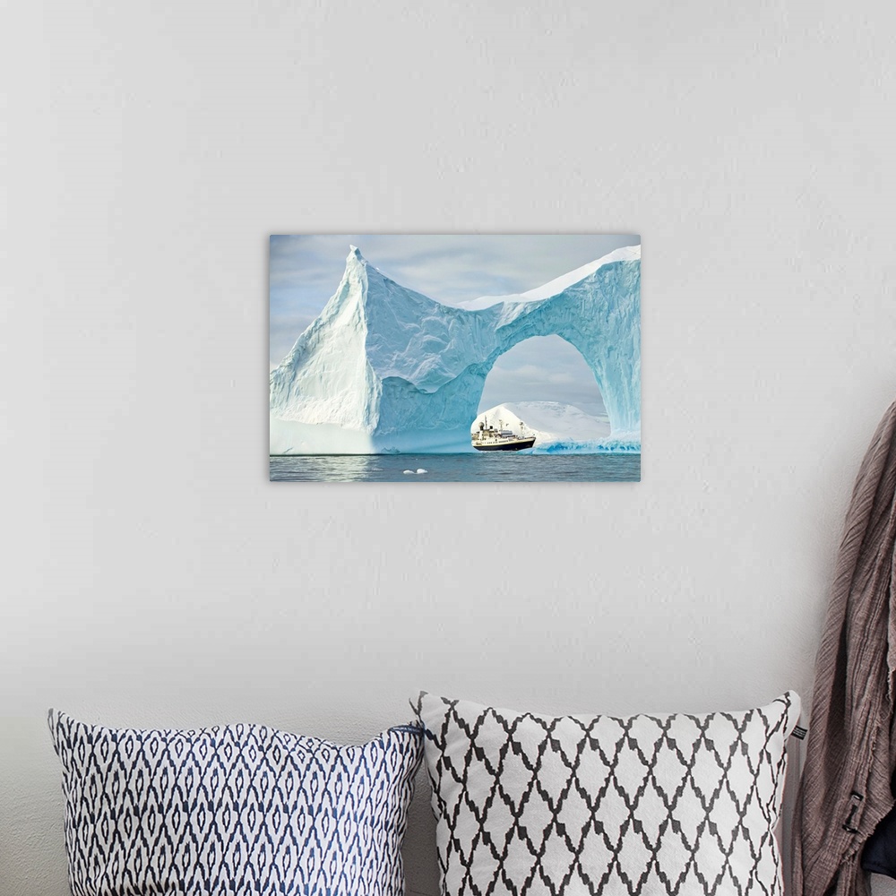 A bohemian room featuring Iceberg with arch frames an expedition ship in the Yalour Islands of Antarctica, Yalour Islands, ...