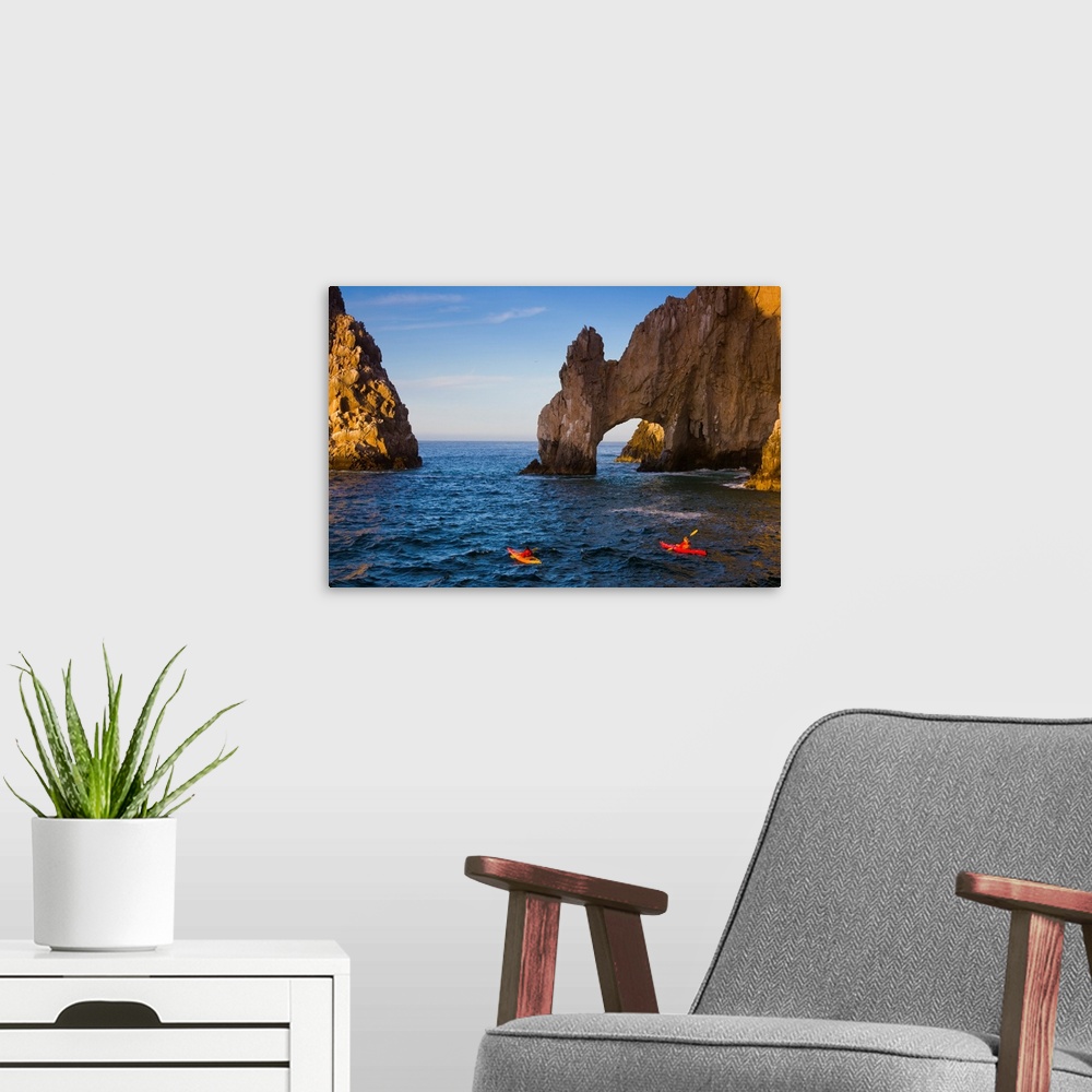 A modern room featuring Two people in kayaks paddle in the ocean near tall rock arch formations.