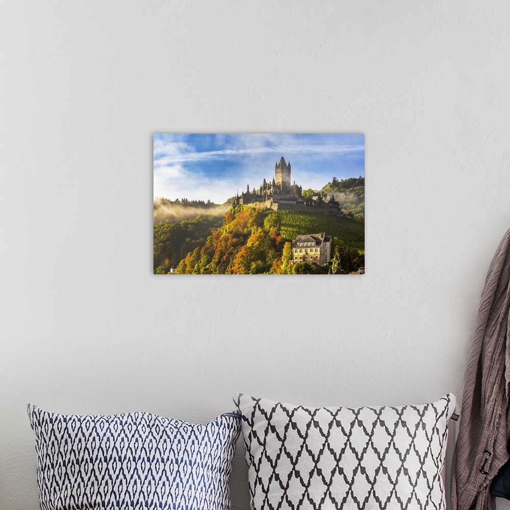 A bohemian room featuring Large medieval castle on a colorful tree hillside with fog, blue sky, and cloud, Cochem, Germany.