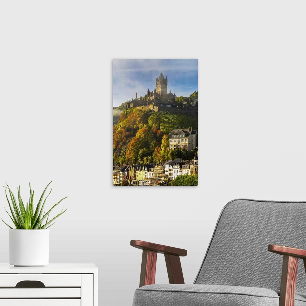 A modern room featuring Large medieval castle on top of a colorful treed hillside with fog, blue sky, cloud, and village ...