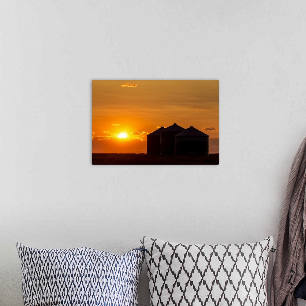 A bohemian room featuring Silhouette of large metal grain bins at sunrise with orange sun rising over clouds; Alberta, Canada