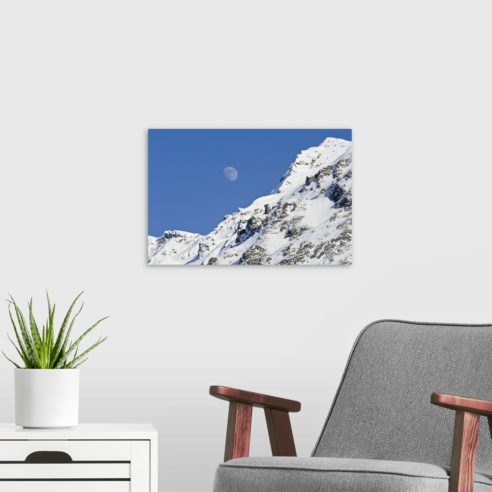 A modern room featuring Moon rising over snow covered mountain peak at Hatcher Pass in Southcentral Alaska.