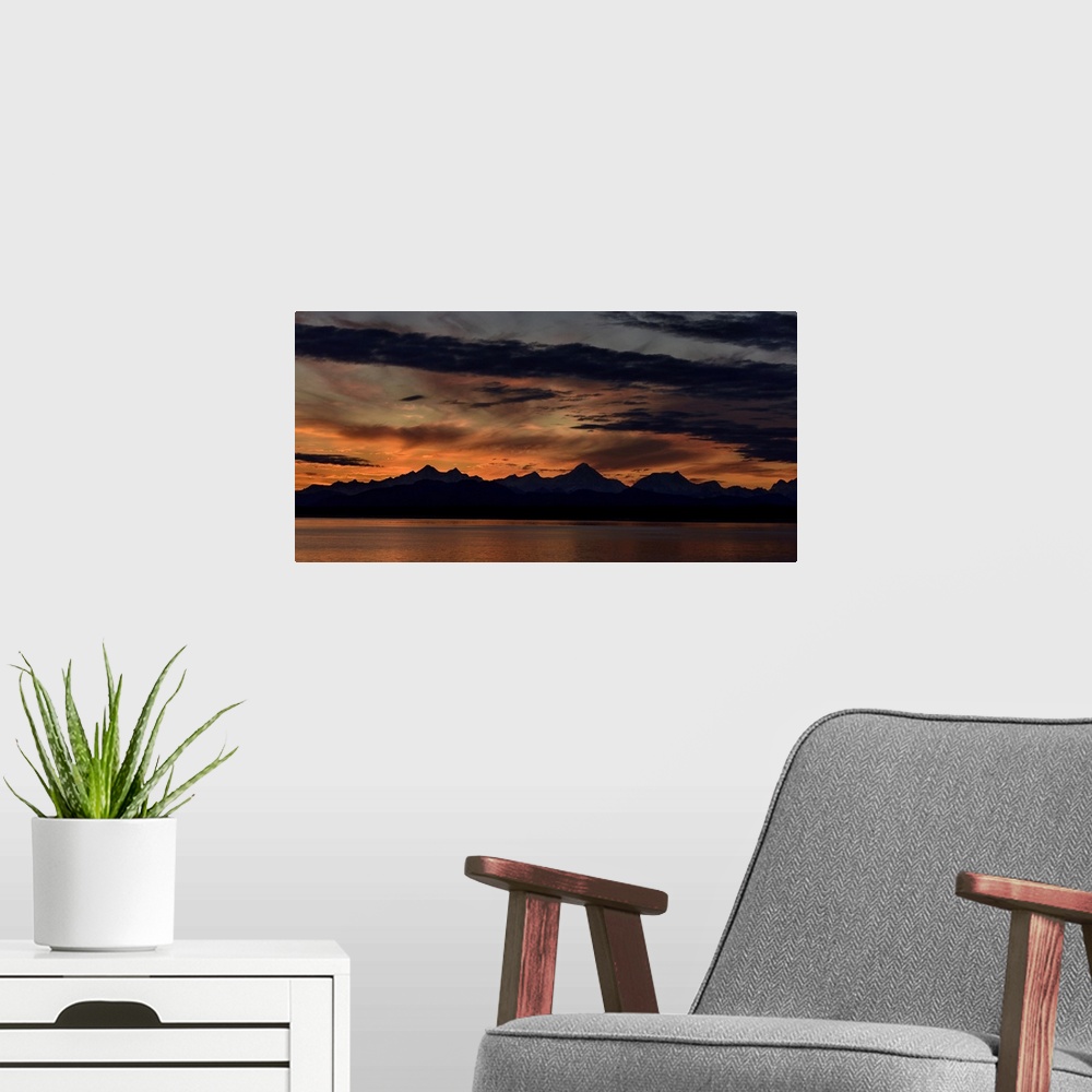A modern room featuring Mountain peaks silhouetted at sunrise, with a dramatic red glowing sky with dark clouds in Glacie...