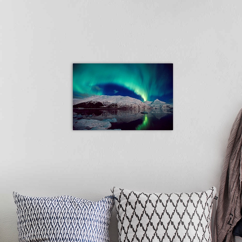 A bohemian room featuring Canvas photo art of northern lights in the sky above snow covered mountains near water.