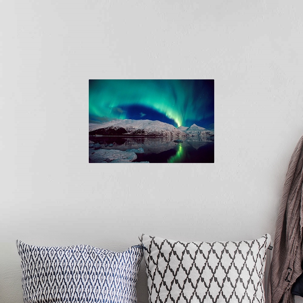 A bohemian room featuring Canvas photo art of northern lights in the sky above snow covered mountains near water.