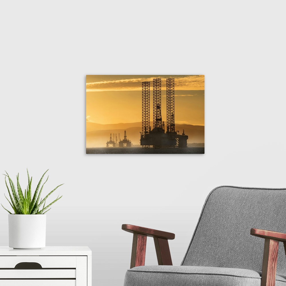 A modern room featuring Oil drilling rigs out in the ocean with a view of the coastline and golden sunset; Cromarty, Inve...