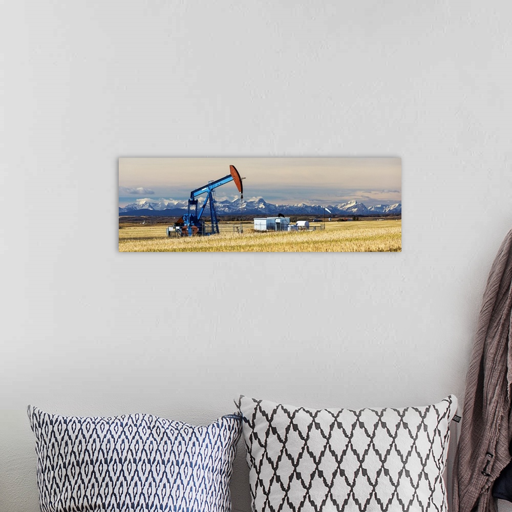 A bohemian room featuring Panorama of a colourful pump jack in cut canola stubble field with snow capped mountains, blue sk...