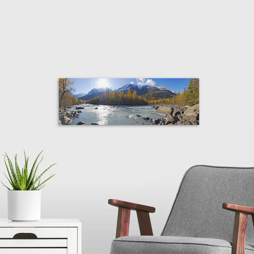 A modern room featuring A photograph of a river running through the Alaskan landscape in lined with trees on a sunny day ...