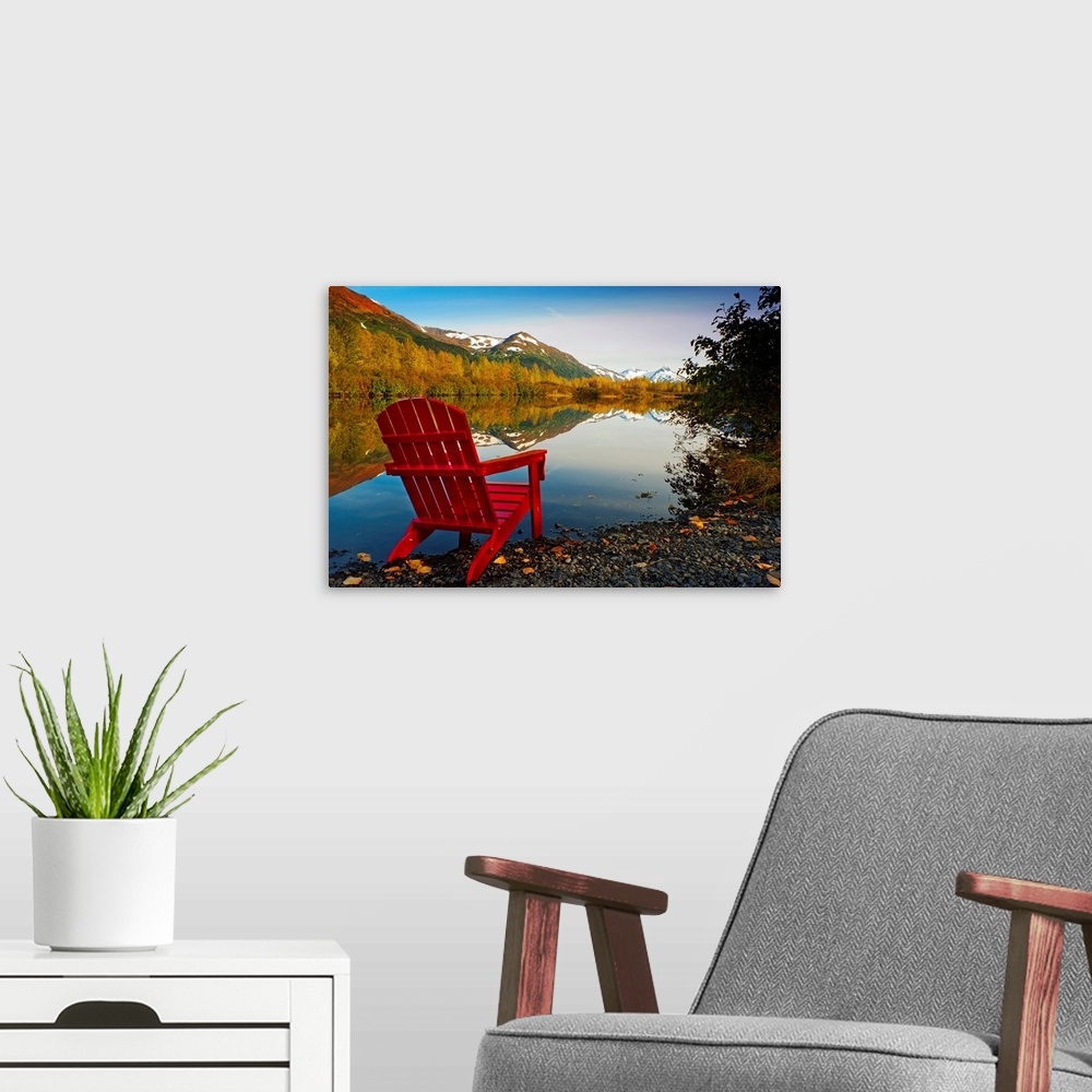 A modern room featuring Landscape photograph on a big canvas of a red Adirondack chair sitting at the edge of a lake that...