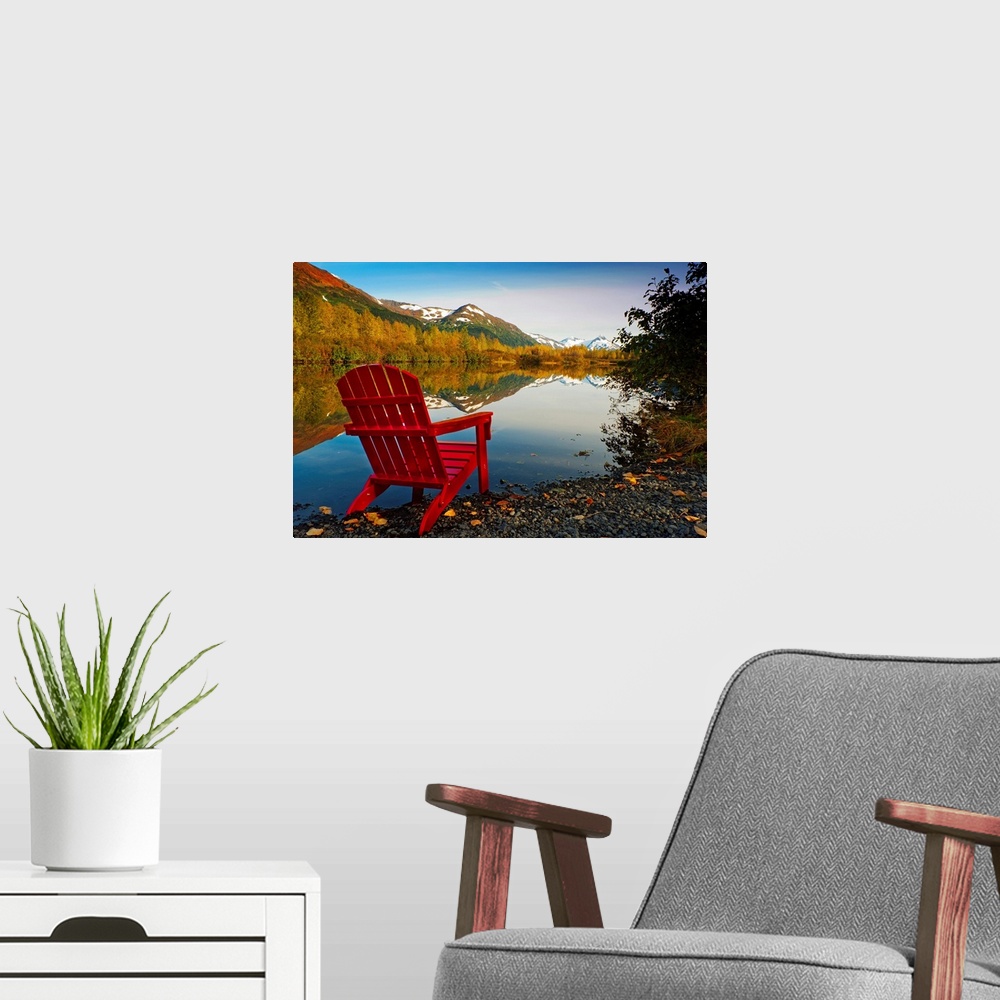 A modern room featuring Landscape photograph on a big canvas of a red Adirondack chair sitting at the edge of a lake that...