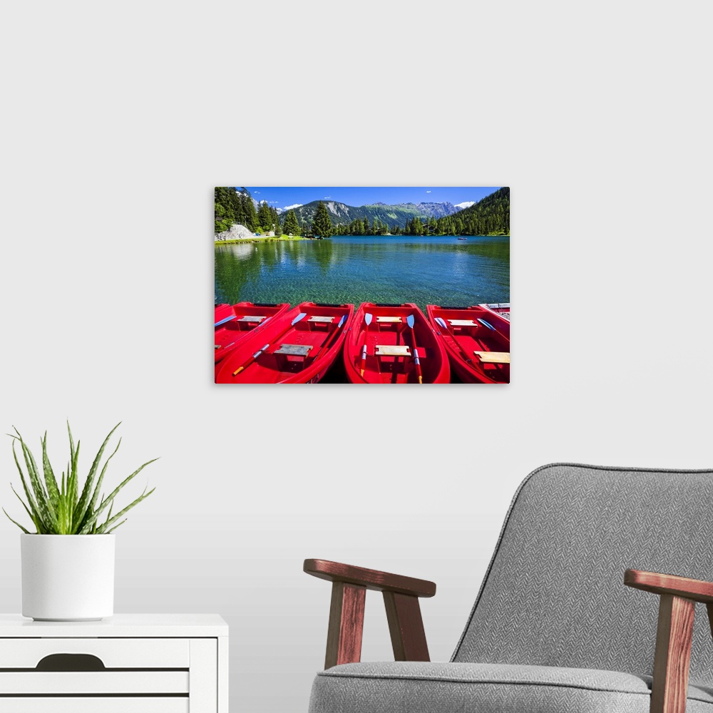 A modern room featuring Red boats lined up at Champex Lake under blue sky with a mountain range in the background; Champe...