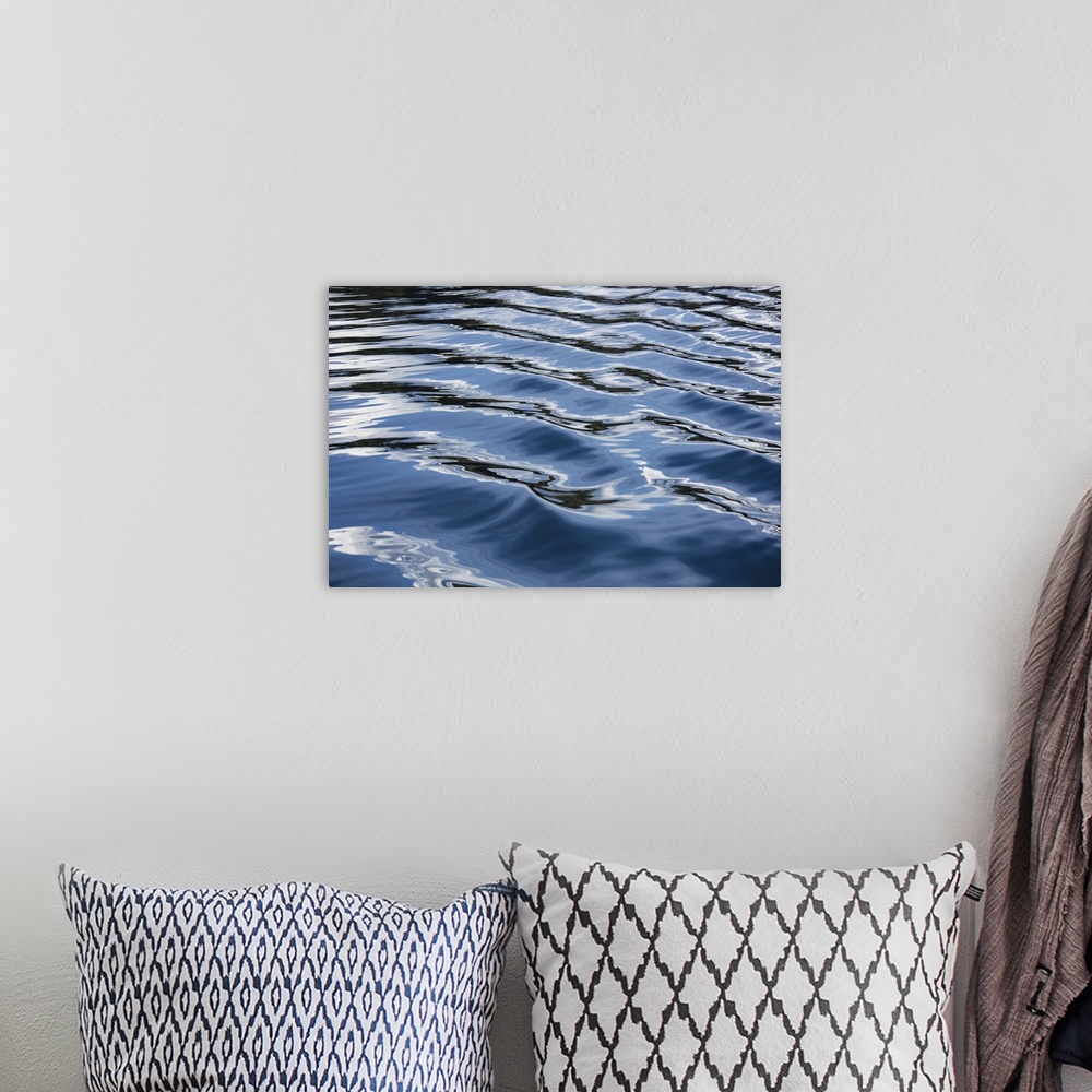 A bohemian room featuring The blue, black, and white reflections of the sky, clouds, and nearby land on the wake of a boat ...
