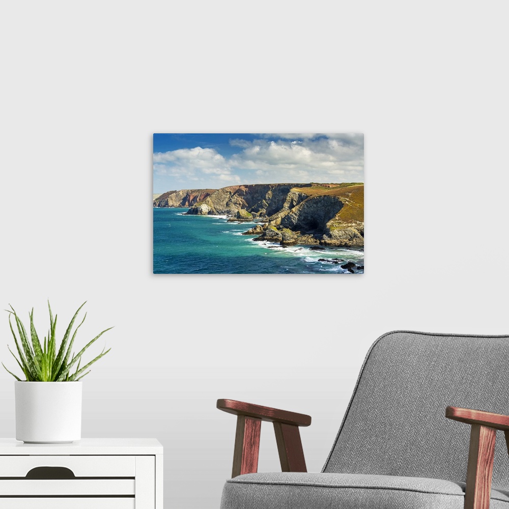 A modern room featuring Rocky cliffs along the shoreline with clouds and blue sky; Cornwall County, England.