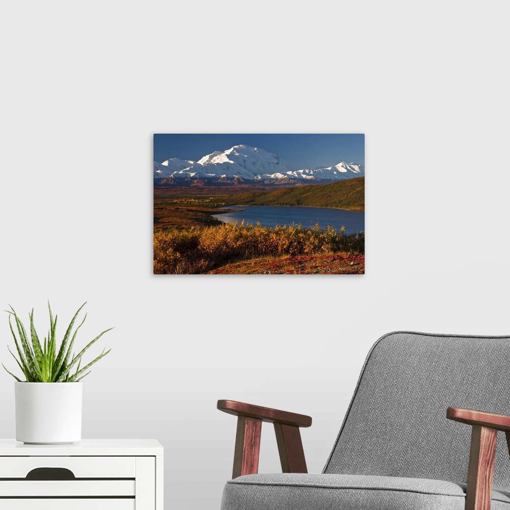 A modern room featuring Large photo on canvas of snow covered mountains in the distance and layers of forests by a lake i...