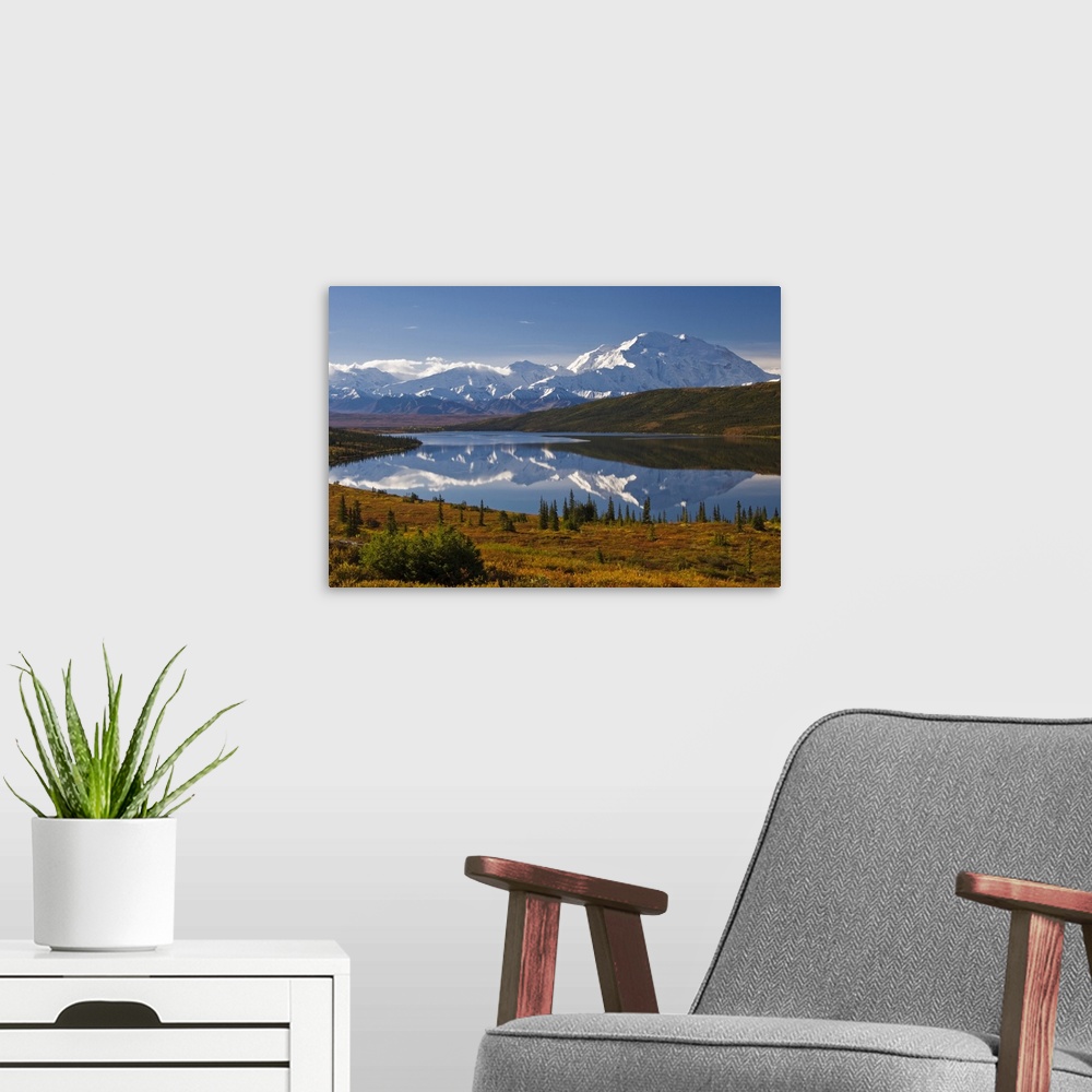 A modern room featuring Photograph of lake surrounded by grassy hills, trees, and bushes with snow covered mountains in t...