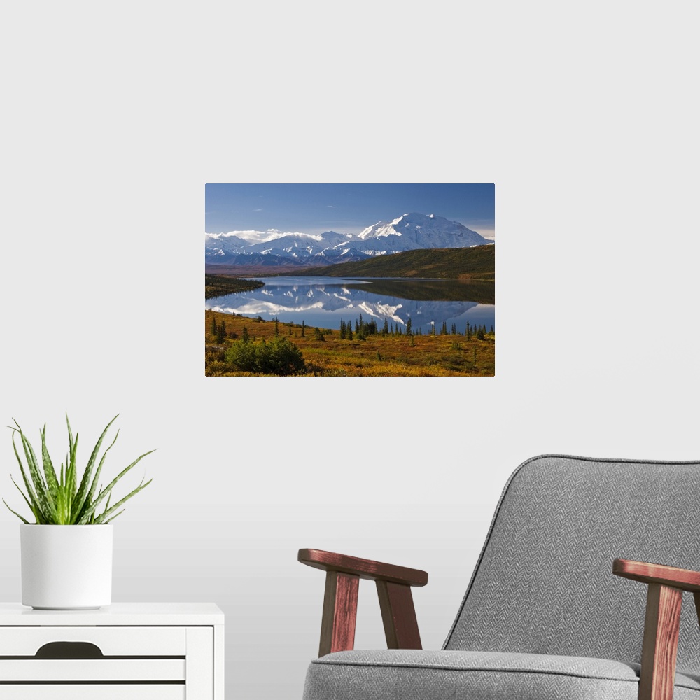 A modern room featuring Photograph of lake surrounded by grassy hills, trees, and bushes with snow covered mountains in t...