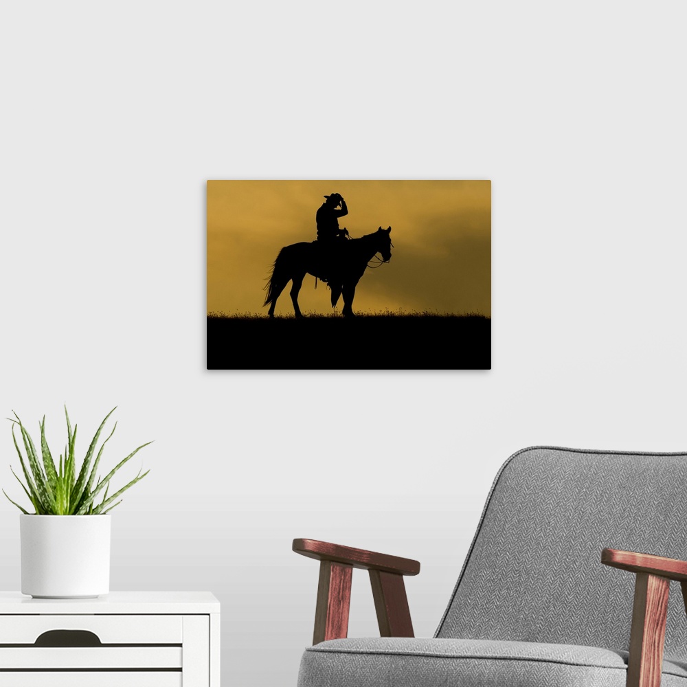 A modern room featuring Silhouette of a cowboy on a horse against a sky of golden cloud at sunset; Montana, United States...