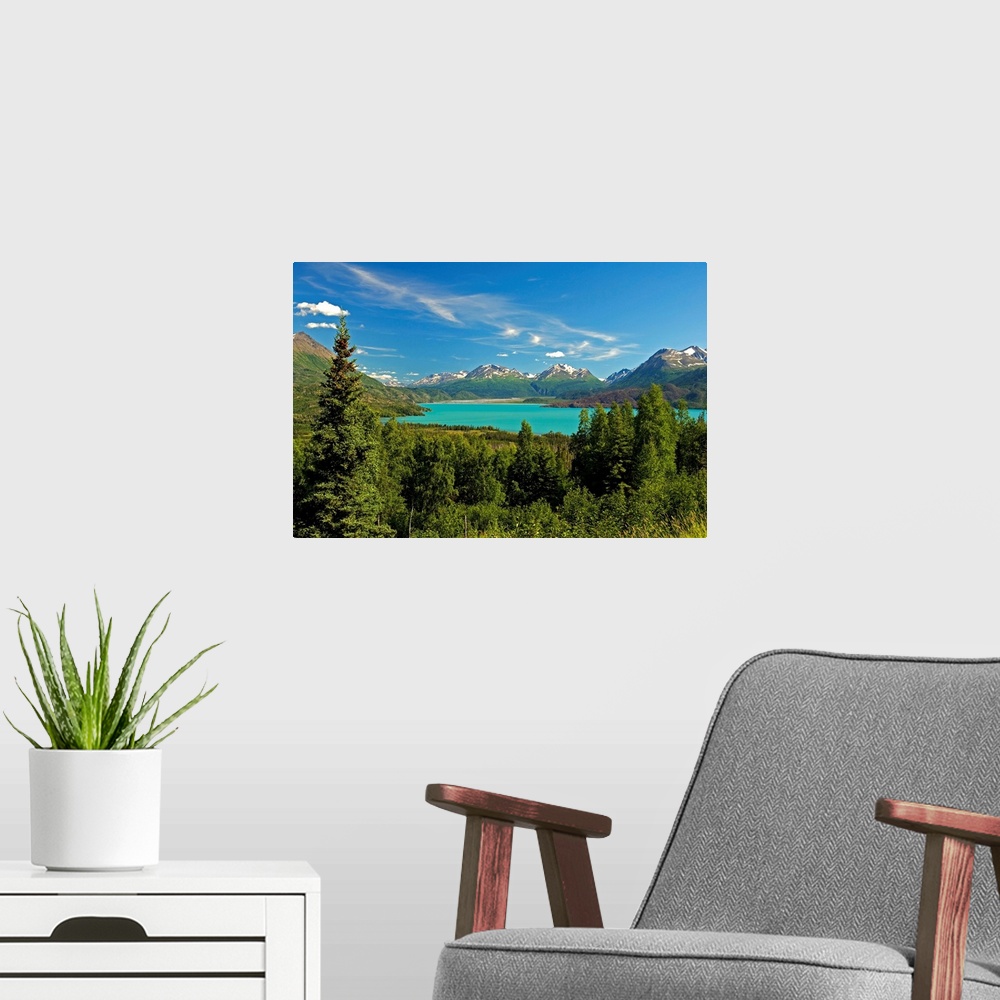 A modern room featuring Large canvas photo art of a forest surrounding a clear lake with snowcapped mountains in the dist...