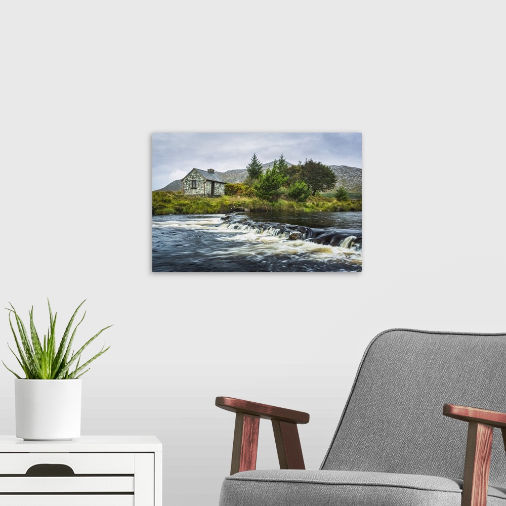 A modern room featuring Small stone fisherman's hut on the banks of a small river with mountains in the background on a c...