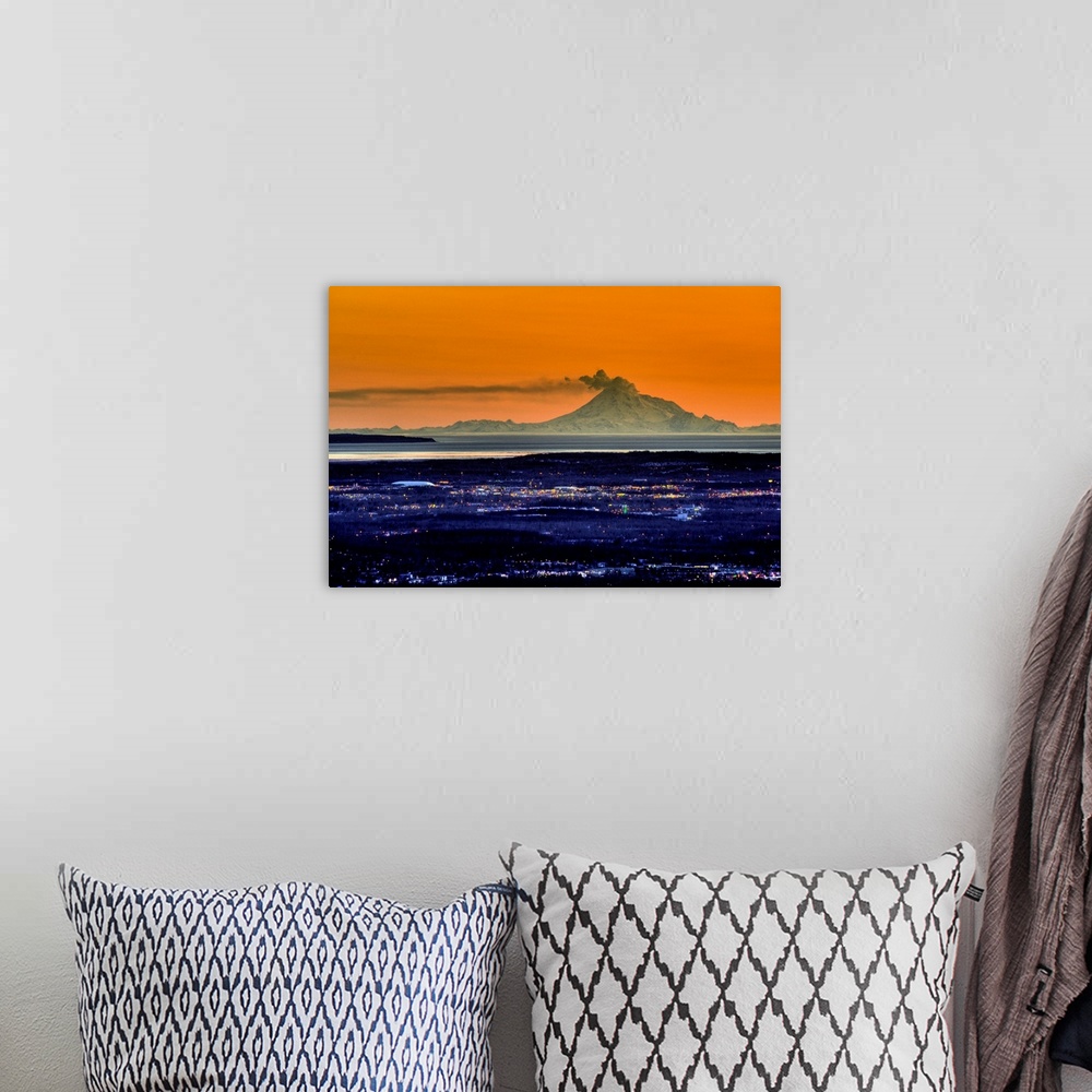 A bohemian room featuring Ash billows out of an active volcano which looms over a city in the evening in the Aleutian mount...
