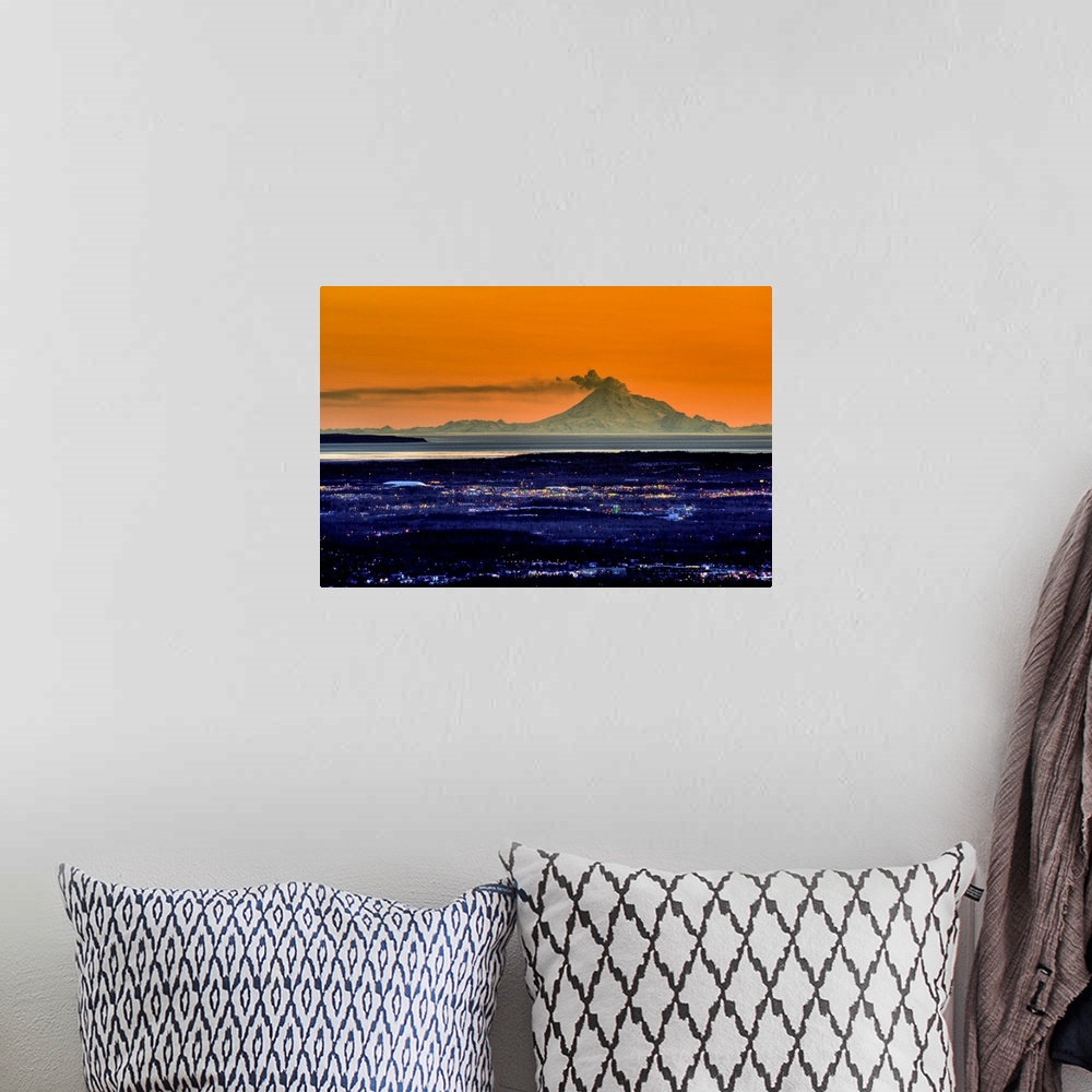 A bohemian room featuring Ash billows out of an active volcano which looms over a city in the evening in the Aleutian mount...
