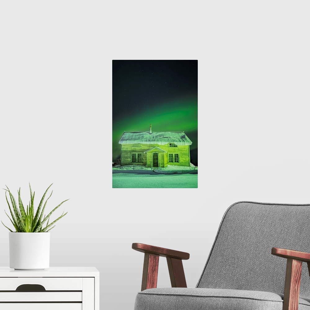 A modern room featuring The Northern Lights in the sky above 'Our Lady of the Snows' Catholic Mission Building in winter,...