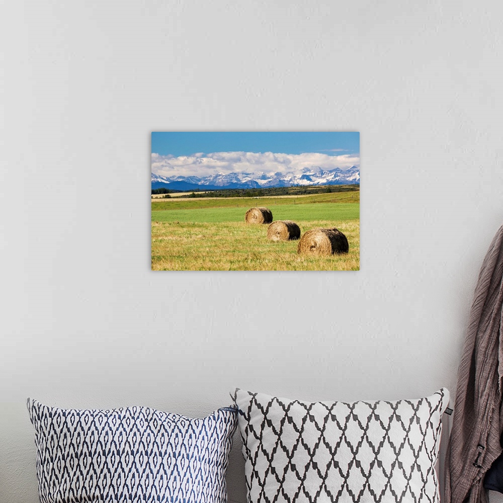 A bohemian room featuring Three hay bales in a field with mountains in the background slightly snow covered and cloudy with...
