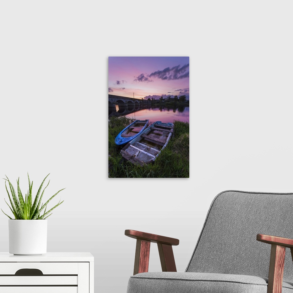 A modern room featuring Two old wooden boats on the banks of the Shannon River at sunset with a stone bridge in the backg...