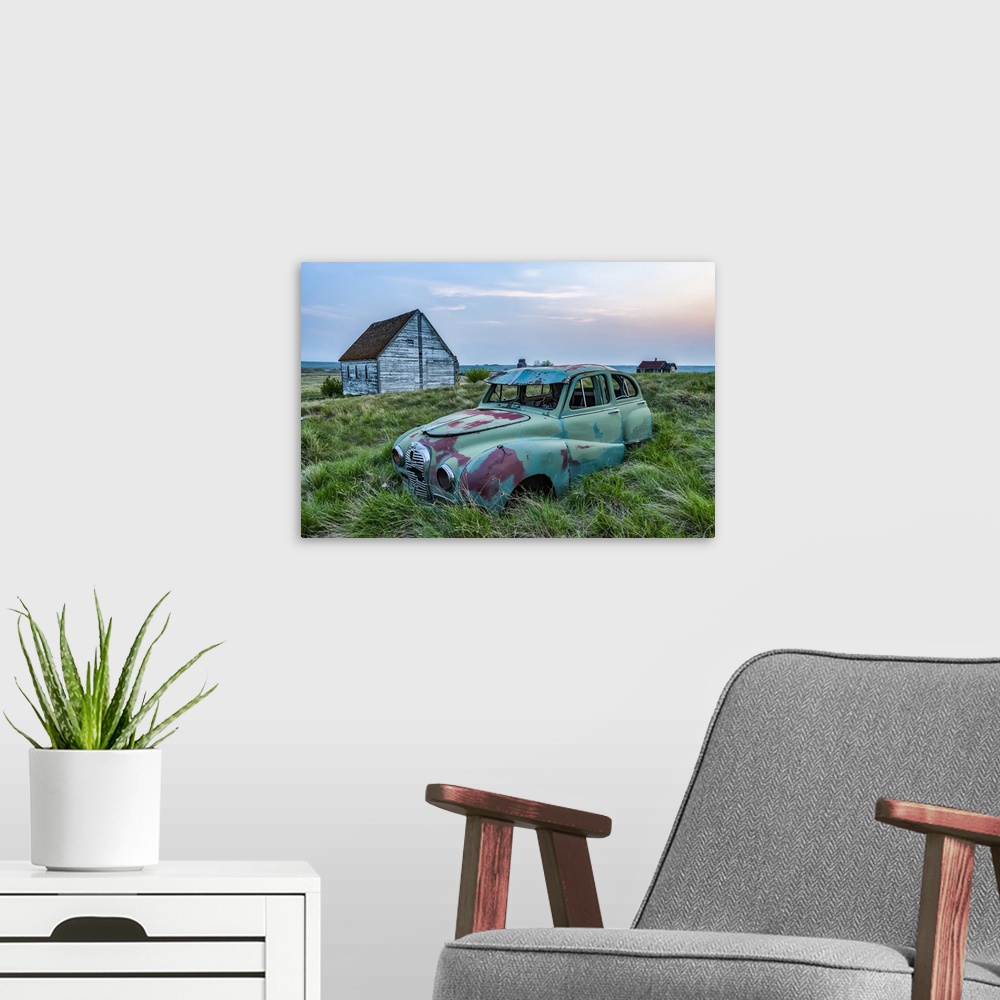 A modern room featuring Vintage car sitting in the overgrown grass in a field with old buildings on a farmstead; Saskatch...