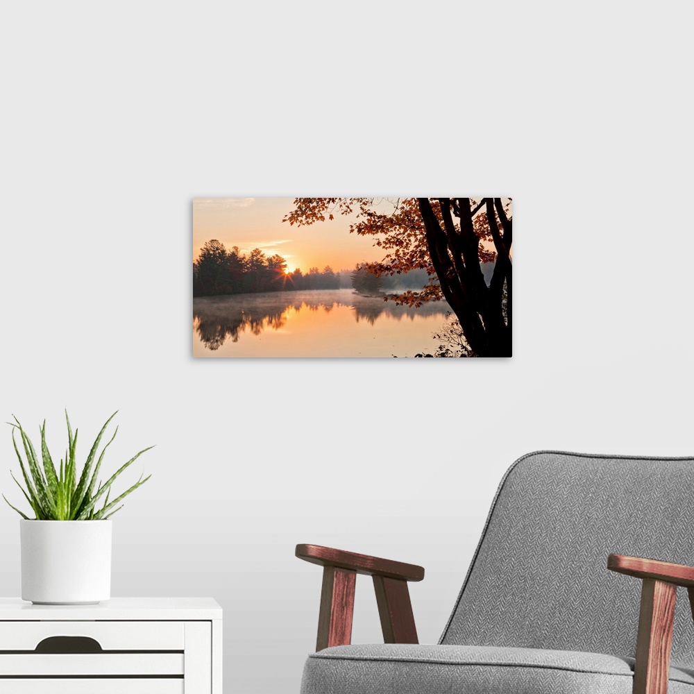 A modern room featuring Big Canvas photo of a tranquil lake at sunrise with forests around it bathed in warm sunlight.
